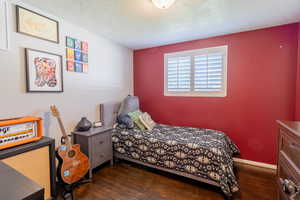 Bedroom with dark wood-style floors, a textured ceiling, and baseboards