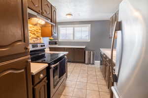 Kitchen featuring stainless steel appliances, under cabinet range hood, light countertops, and decorative backsplash