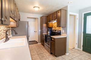 Kitchen featuring stainless steel range with electric cooktop, under cabinet range hood, a sink, light countertops, and decorative backsplash