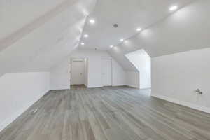 Bonus room featuring light wood-style flooring, baseboards, vaulted ceiling, recessed lighting, and a textured ceiling