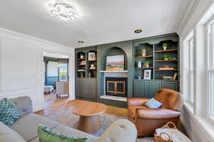 Living area featuring ornamental molding, a tiled fireplace, light wood-type flooring, and built in shelves