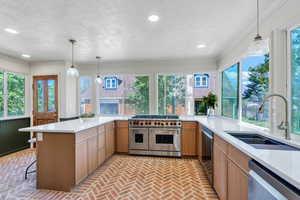 Kitchen with appliances with stainless steel finishes, a sink, brick flooring, light countertops, and a peninsula