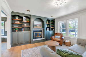 Living area featuring a tile fireplace, healthy amount of natural light, crown molding, light wood finished floors, and a textured ceiling