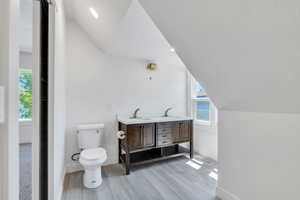 Bathroom featuring baseboards, vaulted ceiling, wood finished floors, plenty of natural light, and toilet