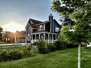Back of house featuring covered porch, a lawn, and a chimney
