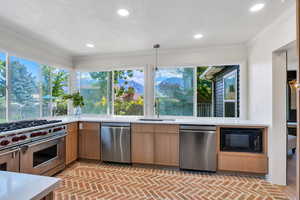 Kitchen with stainless steel appliances, a sink, brick floors, light countertops, and healthy amount of natural light