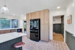 Kitchen featuring black appliances, a sink, light brown cabinetry, brick floors, and ornamental molding
