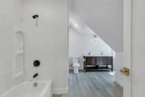 Full bathroom featuring baseboards, toilet, wood finished floors, lofted ceiling, and bathing tub / shower combination