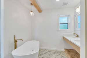 Primary bathroom with a freestanding bath, marble look tiles, beamed ceiling, baseboards, and double vanity