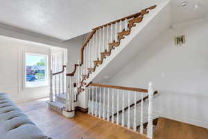 Staircase with wood finished floors, baseboards, ornamental molding, and a textured ceiling