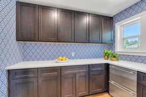 Kitchen featuring wallpapered walls, light countertops, and dark brown cabinets
