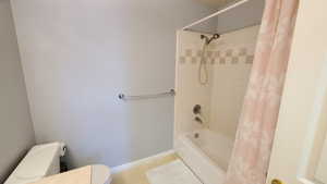 Bathroom featuring toilet, shower / tub combo with curtain, tile patterned flooring, and baseboards