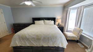 Bedroom with light colored carpet, multiple windows, ornamental molding, baseboards, and a ceiling fan