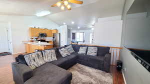 Living area featuring lofted ceiling, ceiling fan, light wood-style floors, and baseboards