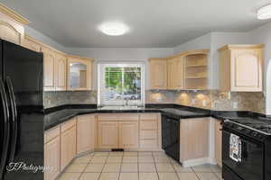 Kitchen featuring black appliances, light brown cabinets, a sink, light tile patterned flooring, and backsplash