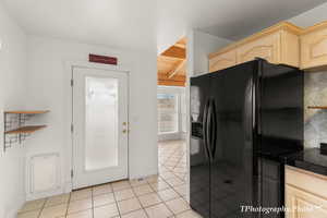 Kitchen with black refrigerator with ice dispenser, light brown cabinets, beamed ceiling, light tile patterned floors, and baseboards