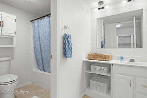 Bathroom with toilet, vanity, baseboards, shower / bath combination with curtain, and tile patterned flooring