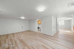Finished below grade area featuring washer / dryer, light wood-style floors, baseboards, and a textured ceiling