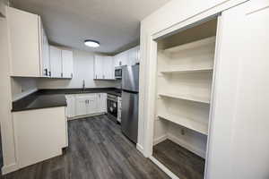 Kitchen featuring stainless steel appliances, a textured ceiling, white cabinetry, and dark wood-type flooring