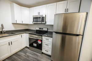 Kitchen featuring appliances with stainless steel finishes, a sink, dark wood-type flooring, dark countertops, and white cabinetry
