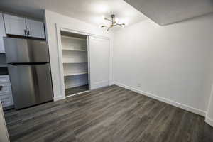 Unfurnished dining area featuring a chandelier, dark wood-style floors, a textured ceiling, and baseboards