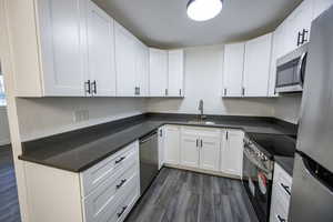 Kitchen featuring appliances with stainless steel finishes, a sink, dark wood-type flooring, white cabinetry, and dark countertops