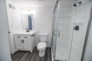 Bathroom with wood finished floors, a shower stall, toilet, and vanity