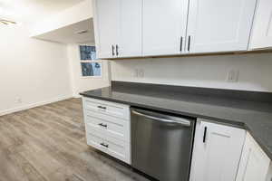 Kitchen featuring dishwasher, white cabinets, wood finished floors, dark stone countertops, and baseboards