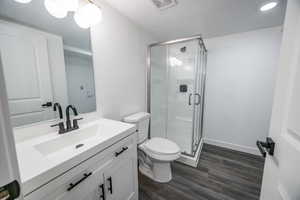 Full bath with vanity, toilet, wood finished floors, a stall shower, and a textured ceiling