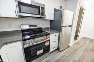 Kitchen with stainless steel appliances, light wood-style flooring, white cabinetry, and dark stone countertops