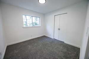 Unfurnished bedroom with dark colored carpet, a closet, and baseboards