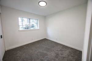Empty room featuring dark carpet and baseboards