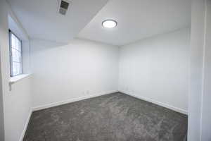 Spare room featuring dark colored carpet and baseboards