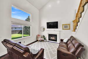 Living room featuring high vaulted ceiling, wood finished floors, a glass covered fireplace, stairs, and baseboards
