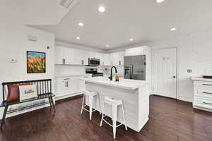 Kitchen featuring stainless steel appliances, light countertops, a breakfast bar area, dark wood finished floors, and recessed lighting