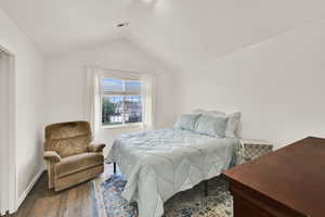 Bedroom with vaulted ceiling, wood finished floors, and baseboards
