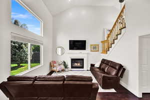 Living area featuring high vaulted ceiling, wood finished floors, stairway, a glass covered fireplace, and baseboards