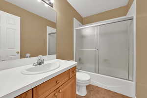 Bathroom with toilet, vanity, tile patterned floors, and combined bath / shower with glass door