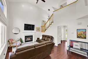 Living room with a glass covered fireplace, high vaulted ceiling, a ceiling fan, stairway, and dark wood-style floors