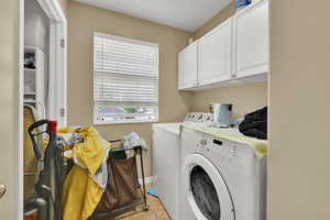 Clothes washing area featuring independent washer and dryer, cabinet space, and light tile patterned floors