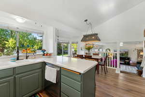 Kitchen with green cabinetry, a sink, dishwasher, a peninsula, and vaulted ceiling