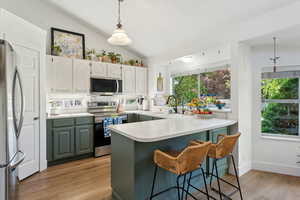 Kitchen with appliances with stainless steel finishes, a peninsula, a sink, lofted ceiling, and light wood-type flooring