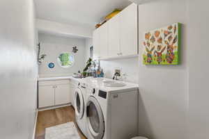 Laundry area featuring separate washer and dryer, light wood-style floors, and cabinet space