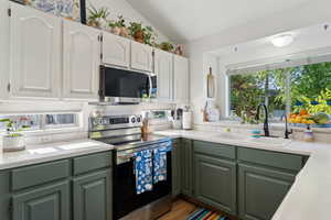Kitchen featuring stainless steel appliances, a sink, green cabinets, light countertops, and vaulted ceiling