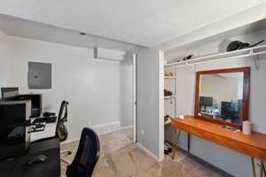 Carpeted office with electric panel, a textured ceiling, and baseboards