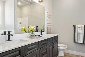 Bathroom featuring wood finished floors, toilet, double vanity, and baseboards