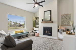 Living room with a glass covered fireplace, a ceiling fan, wood finished floors, and vaulted ceiling