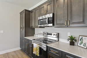 Kitchen featuring appliances with stainless steel finishes, light countertops, baseboards, light wood finished floors, and dark brown cabinetry