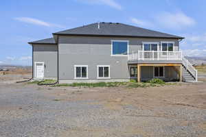 Rear view of house with a deck, stairway, stucco siding, and roof with shingles