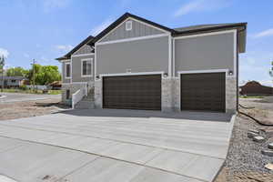 View of property exterior with concrete driveway, board and batten siding, a garage, and stone siding